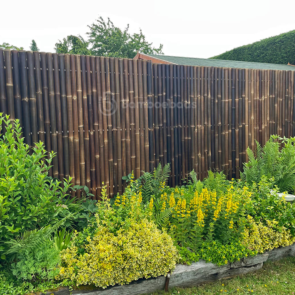 Donkerbruine bamboe schutting Giga als erfafscheiding met veel planten